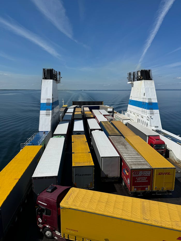 Rows of cargo trucks loaded on a ferry ship crossing the sea under a clear sky.